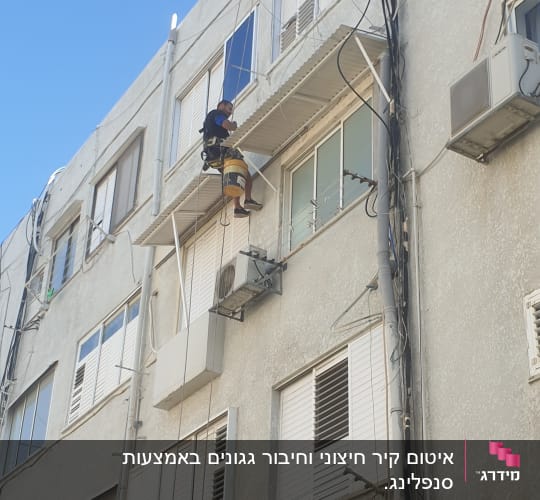 אדם תלוי על חבל מבצע עבודת איטום על קיר בניין